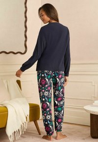 Marineblauwe longsleeve top met een losse pasvorm, gecombineerd met pyjamabroek met patroon in zwart, voorzien van levendige bloemenontwerpen in roze, teal en wit.