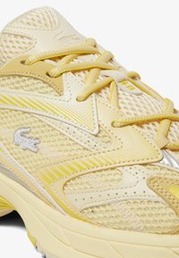 Gelbe Mesh-Sneaker mit einer strukturierten Oberseite, einfarbigen gelben Schnürsenkeln, reflektierenden Akzenten und einem dezenten Logo an der Seite.