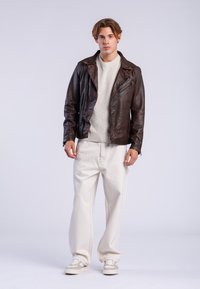 Veste de moto en cuir marron, pull en tricot gris clair, pantalon surdimensionné blanc et baskets crème. Tenue décontractée en couches avec des couleurs contrastées.