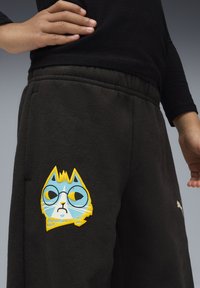 Sorte sweatpants med et trykt design af en tegneserie-kat iført briller, i lyseblå, gul og hvid farve. Elastisk talje.