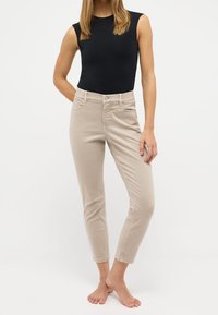 Pantalones recortados beige de corte ajustado, hechos de una suave mezcla de algodón. Presentan bolsillos delanteros, cierre de botón y detalles de costura sutiles.