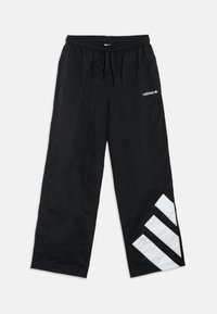 Čierne teplákové nohavice Adidas s elastickým pásom, šnúrkou na utiahnutie, bočnými vreckami, bielym logom na bokoch a veľkými bielymi pruhmi pri spodnom leme ľavej nohy.