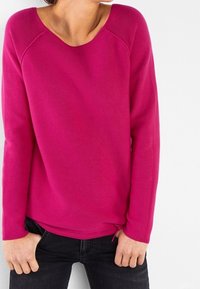 Suéter de punto rosa con un escote redondo, mangas largas tipo raglán y un dobladillo ligeramente corto. Tejido texturizado con un ajuste casual.