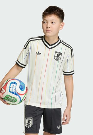 Garçon portant un maillot et un short de football du Japon, tenant un ballon de football FIFA multicolore, regardant sur le côté sur un fond uni.
