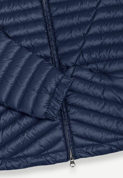 Navy blue quilted jacket with horizontal and diagonal stitching, a front zipper partially unzipped, and a cuffed sleeve visible.