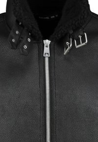 Zwarte faux leren jas met een gestructureerde afwerking, voorzien van een rits aan de voorkant, met gespsluitingen bij de kraag en een zachte, faux bont voering.