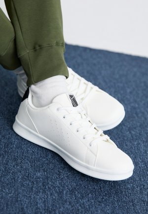 White sneakers made of smooth synthetic material, featuring perforated design accents, black heel tab, and flat white rubber sole.