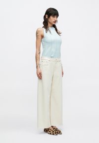Top azul claro sin mangas con costuras verticales, combinado con pantalones anchos color crema. Zapatos con estampado de leopardo completan el conjunto.