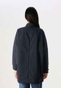 Veste ample et sombre, fabriquée en tissu lisse et résistant à l'eau. Caractérisée par un col haut et un design de dos parfaitement ajusté.
