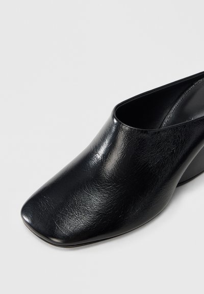 Μαύρα δερμάτινα mules με τακούνι, λεία υφή, τετράγωνη μύτη και καμπυλωτό τακούνι. Ο σχεδιασμός διαθέτει ανοιχτή πλάτη για εύκολη εφαρμογή.