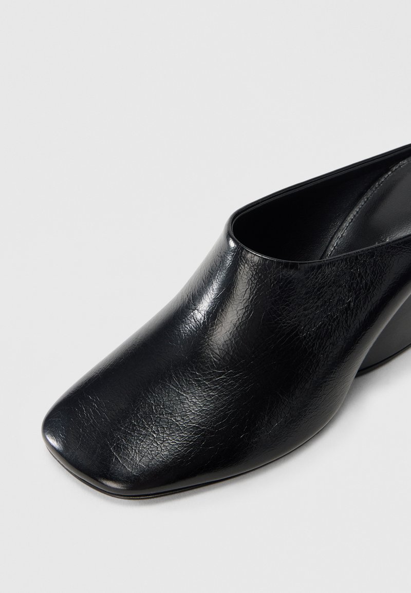 Schwarze Leder-Mules mit Absatz, glatter Textur, quadratischer Zehenpartie und schmal zulaufendem Absatz. Das Design verfügt über eine offene Ferse für einfaches An- und Ausziehen.
