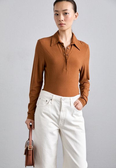 Polo à manches longues côtelé marron avec patte de boutonnage, associé à un pantalon large taille haute blanc et un petit sac à main marron.