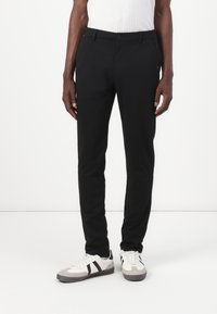 Sorte slim-fit bukser laget av glatt stoff, med knappelukking og beltehemper, kombinert med hvite og grå treningsko med svarte striper.