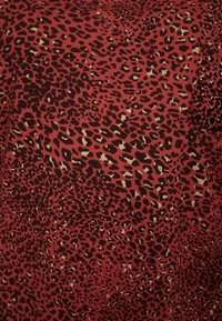 Röd tyg med ett mönster av leopardtryck i svarta och beige fläckar, med en slät textur och ett något stretchigt utseende.