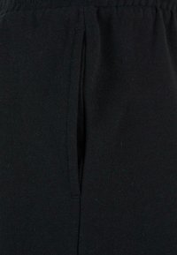 Pantaloni de trening negri, confecționați dintr-un material moale, elastic din bumbac, cu deschidere pentru buzunar lateral și detalii cu talie elastică.
