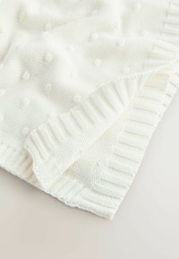 White knitted blanket featuring a textured pattern of small bobbles and a ribbed edge. Soft material with a smooth, even surface.