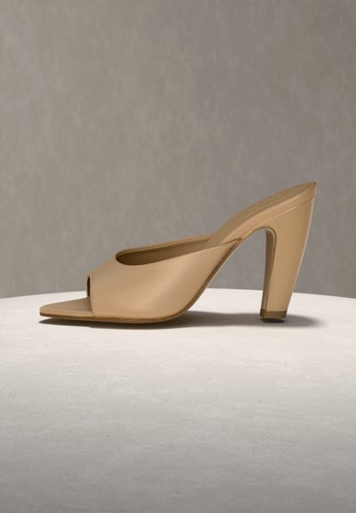 Mule beige à bout ouvert avec un talon haut épais, présenté en profil latéral sur une surface claire avec un fond uni.