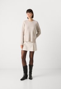 Beige strikket genser med ribbede detaljer, kremfarget skjørt med slit, og svarte lær cowboystøvler. Nøytral fargepalett, uformell stil.