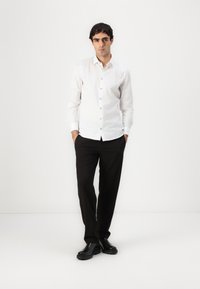 White long-sleeve shirt with a button-down front, paired with black trousers and black shoes; smooth fabric, fitted design, minimal detailing.