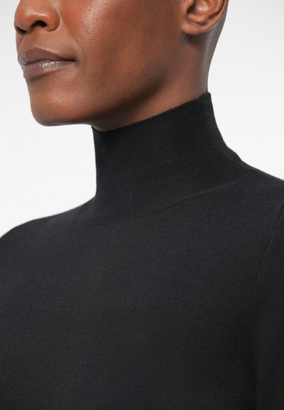 Melna augstās apkakles blūze ar pieguļošu dizainu un ribotu apkakli, izgatavota no mīkstas, teksturētas auduma, ar tīrām līnijām un minimālu apdari.