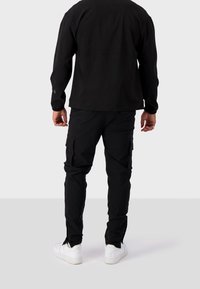 Czarna bluzka z długim rękawem i czarne spodnie cargo z trwałego materiału. Buty są białe z teksturowaną podeszwą. Prosty design z praktycznymi kieszeniami.