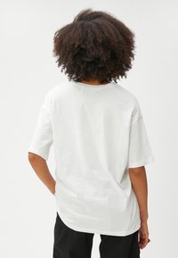 Hvid bomulds T-shirt med en afslappet pasform, korte ærmer, rund halsudskæring og et enkelt design. Bagudsigten viser en glat tekstur og enkelhed.
