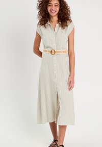 Robe sans manches boutonnée, de couleur vert clair avec des rayures blanches, mettant en avant une taille cintrée et une ceinture beige avec une boucle ronde. Ourlet plat.