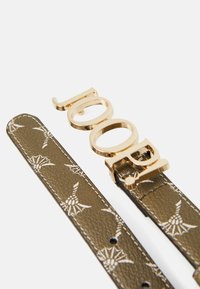 Gold metal belt buckle with the word "LOOK" attached to a textured olive-green strap featuring a white pattern of wings and arrows.