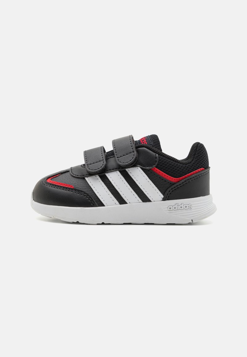 Zapatos de cuero negro con rayas blancas, acentos rojos y bandas de velcro. Punta redondeada, suela acolchada y panel trasero texturizado.