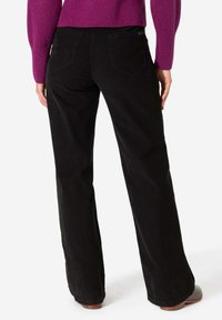 Black corduroy flared pants with a textured finish, featuring two back pockets and a fitted waist, paired with a purple sweater.