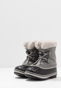 Botas de neve cinzas à prova d'água com um colar de pele de pelo cinza claro, biqueira de borracha e sola texturizada para aderência. Atacadores ajustáveis para um melhor ajuste.