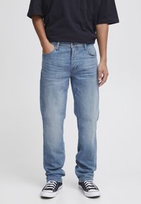 Light blue denim jeans with straight legs, featuring a classic five-pocket design and subtle fading. Paired with black low-top sneakers.