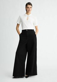 Cămașă albă cu mâneci scurte, cu guler și detaliu în formă de cheie; asociată cu pantaloni negri, cu talie înaltă și picior larg, și pantofi negri cu vârful ascuțit.
