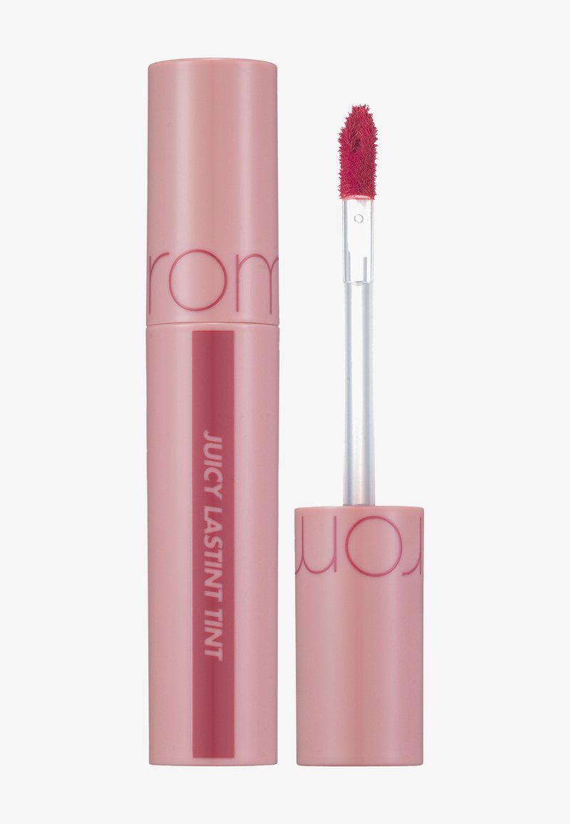 Różowy, cylindryczny pojemnik na pomadkę w płynie z błyszczącym wykończeniem i przezroczystą szczoteczką aplikacyjną; na etykiecie widnieje nazwa produktu w wyraźnej, eleganckiej czcionce.