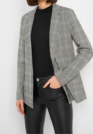 Grau karierter Blazer mit langem Schnitt, leichtem Stoff, Reverskragen und leicht lockerer Passform. Tragen über einem schwarzen Top und schwarzen Hosen.