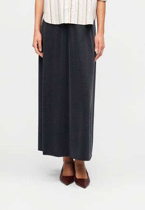 Μακριά φούστα σε σκούρο γκρι, λείο ύφασμα με άνετη εφαρμογή. Συνδυασμένη με ανοιχτό πουκάμισο με κουμπιά και μυτερές μπορντό γόβες.