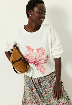 White sweatshirt with pink floral print, paired with a floral skirt in green, pink, and blue tones, and a brown suede shoulder bag.