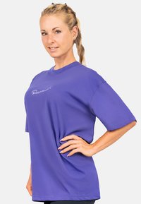 Paars oversized T-shirt van katoen met korte mouwen. Heeft een gestikt logo aan de voorkant. Glad textuur.