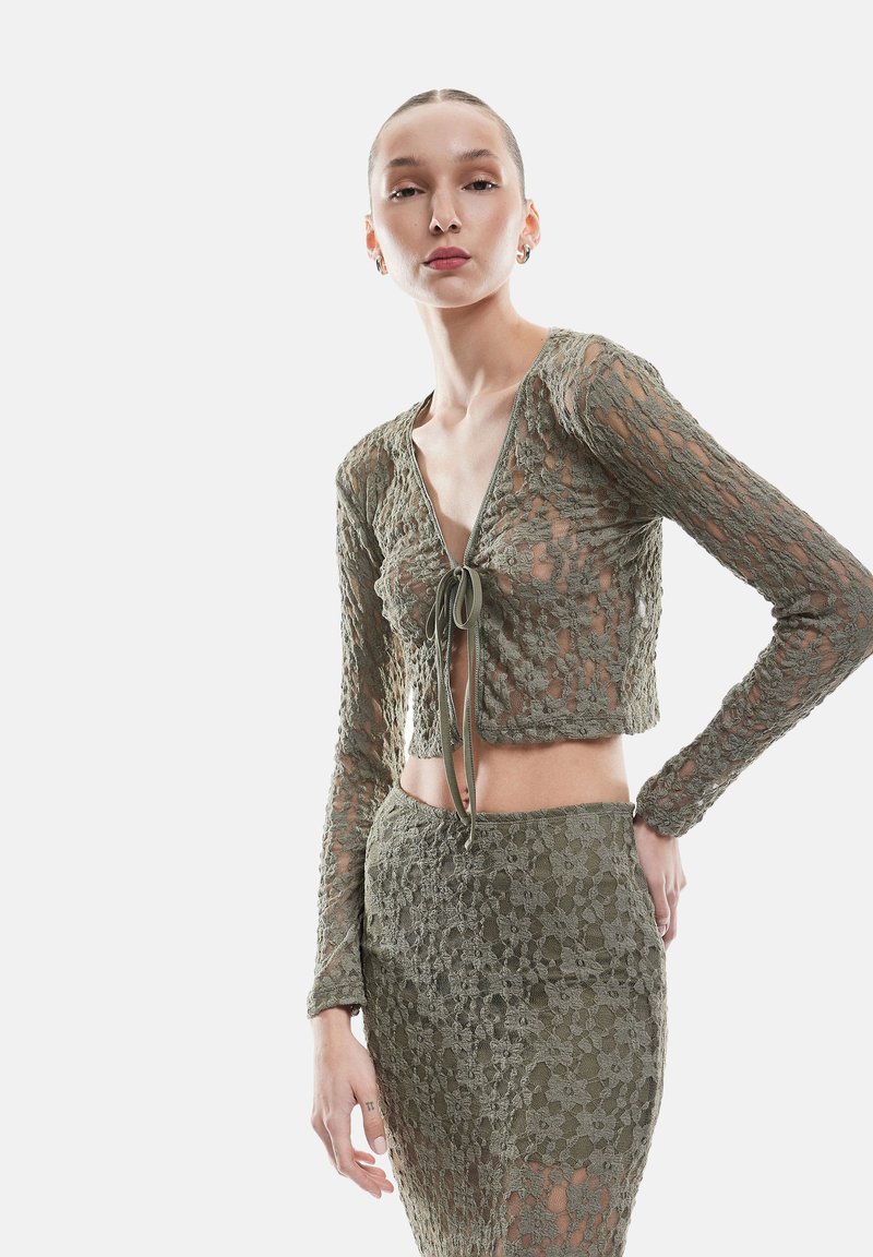 Olijfgroene kanten crop top met lange mouwen, diepe V-hals en sluiting met strik. Gekoppeld aan een aansluitende rok, beide met bloemmotieven.