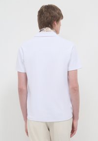 Polo shirt bianca a maniche corte con tessuto testurizzato e colletto classico, con un dettaglio a motivo all'interno del colletto.