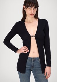 Navy long-sleeve cardigan with a deep V-neck, featuring a front clasp detail. Soft material, fitted cut, and slight texture at edges.