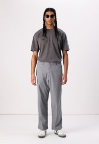 Gray t-shirt with a relaxed fit, paired with light gray wide-leg pants and white sneakers with black stripes. Dark sunglasses complete the look.