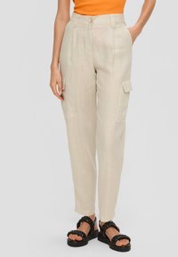 Beige linnen cargobroek met zijzakken, getailleerde pasvorm, hoge taille en opgerolde zoom. G gedragen met zwarte gevlochten sandalen.