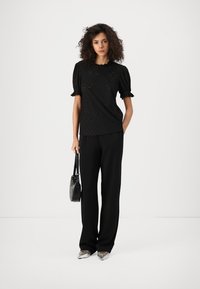 Černý kr short-sleeve top s texturovanou látkou, s rukávy s puffem a jemným vzorem. Nosit s černými kalhotami s širokými nohavicemi a kabelkou.