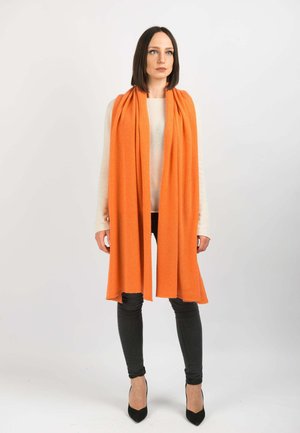 Écharpe orange vif en matériau doux, avec un design long et fluide aux bords bruts, portée sur un pull léger et un jean noir.