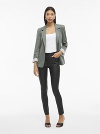 Grijze blazer met opgerolde mouwen, witte tanktop en strakke zwarte broek, met een gladde textuur en minimale accenten. Zwarte open teen hakken.