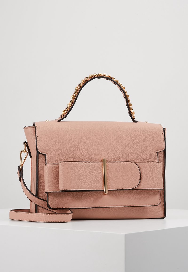 Sac à main rectangulaire en cuir rose clair avec une grande sangle avant, une anse chaîne dorée et une bandoulière amovible sur une surface blanche.