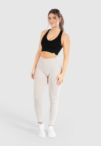Top corto a coste nero abbinato a leggings a vita alta grigi chiari e sneakers bianche, che mostrano un design aderente e elastico.