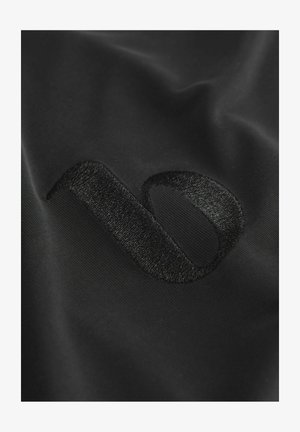 Črn material s teksturiranim, vezenim logotipom v elegantnem, minimalističnem oblikovanju. Površina je gladka s subtilnim sijajem.