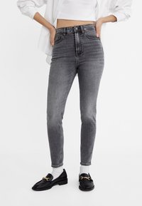 High-waisted, gray jeans with a slim fit, belt loops, and subtle fading. Paired with black loafers and white socks.